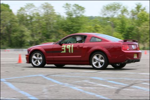 2001 Mercury Grand Marquis - A red Ford Mustang with racing numbers navigates an autocross course on a paved lot.