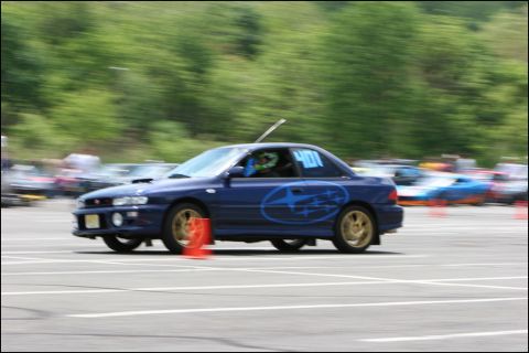2001 Mercury Grand Marquis - Blue Subaru Impreza WRX STI navigates an autocross course with racing decals and gold wheels.
