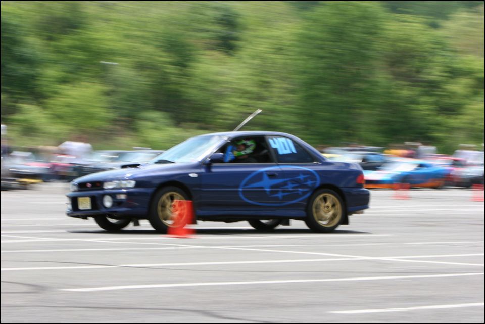 Blue Subaru Impreza WRX STI with gold wheels and large star decals on side, number 401 on window, driving on a track with orange cones