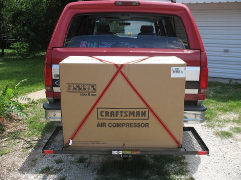 1994 Ford C-150 (Centurion Conversions) - Rear view of a red pickup truck carrying a large box on a cargo carrier.