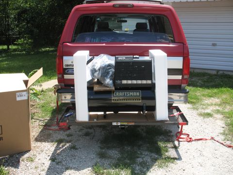 1994 Ford C-150 (Centurion Conversions) - A red 1990s Ford pickup truck is shown from the rear, carrying a Craftsman air compressor on a hitch-mounted carrier.