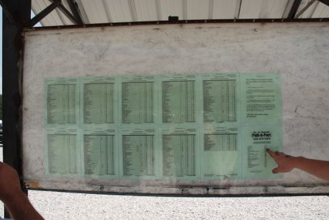 1996 Ford Bronco - Photograph of a self-serve junkyard parts price board with multiple green pricing sheets, not a single classifiable document.