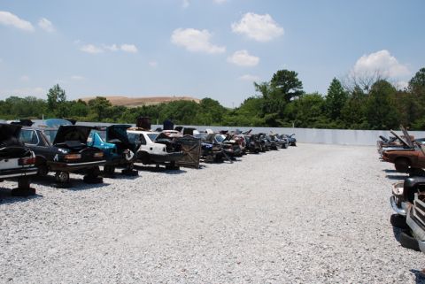 1996 Ford Bronco - A junkyard filled with various vehicles, some with hoods open, under a partly cloudy sky.