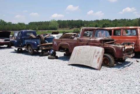 1996 Ford Bronco - A rusty pickup truck sits in a junkyard with its hood removed, alongside other vehicles.