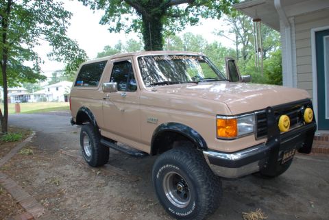 1996 Ford Bronco - This tan Ford Bronco features a bull bar with smiley face fog lights and off-road tires.