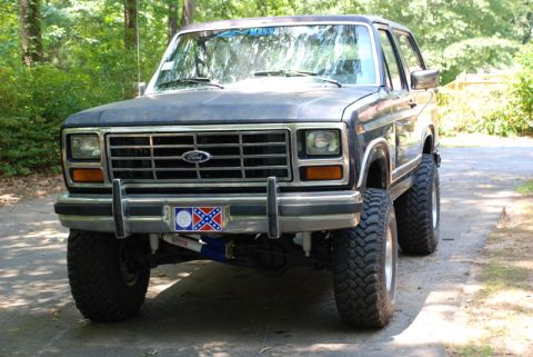 1996 Ford Bronco - This lifted Ford Bronco is parked on a dirt road surrounded by trees.