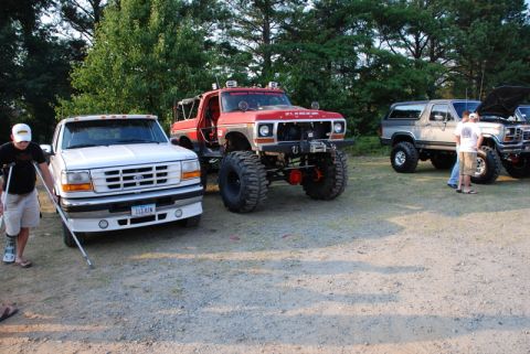 1996 Ford Bronco - Several modified trucks are parked together outdoors on a sunny day.
