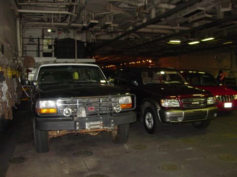1994 Ford Bronco - Three SUVs are parked in a row inside a large, dimly lit structure.
