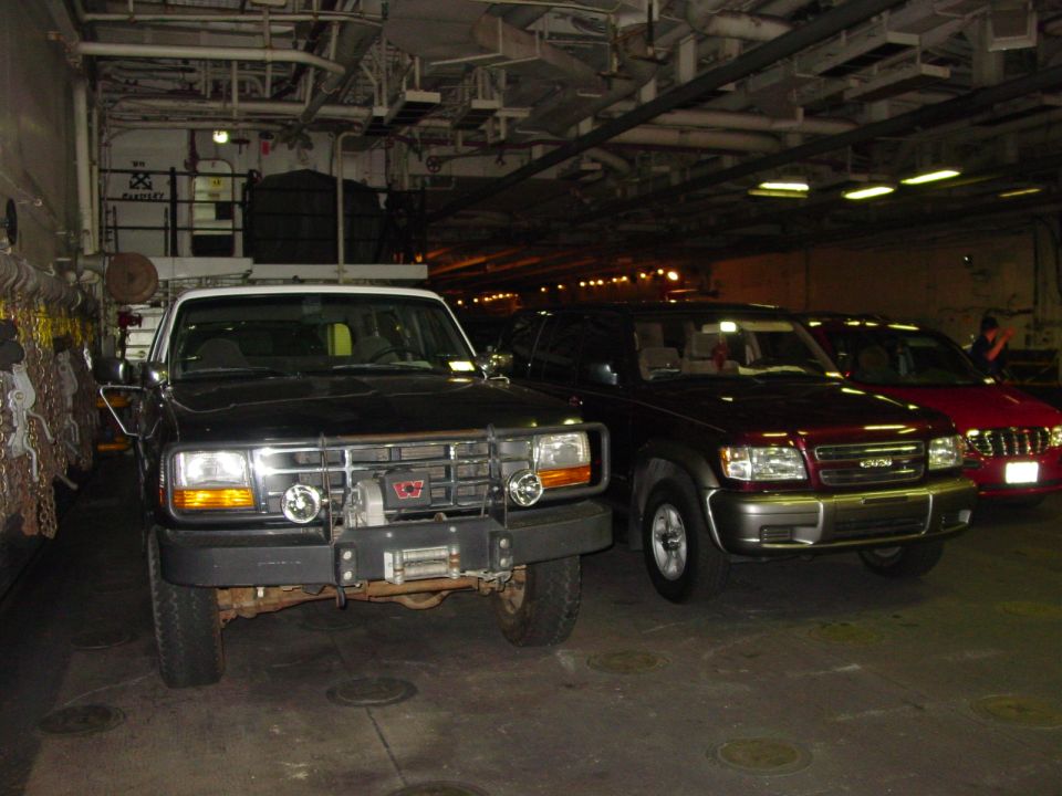 Three SUVs parked inside a large structure; the front vehicle is black with a winch, the middle is maroon, and the rear is red