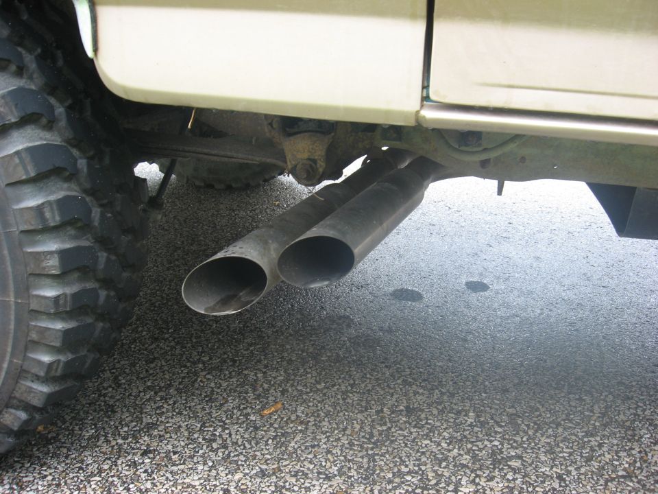 Dual exhaust pipes visible under the side of a vehicle, with a large tire on the left