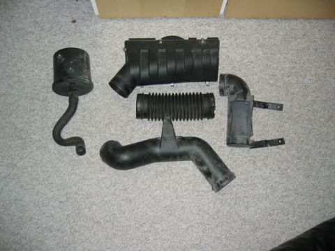 1996 Dodge 2500 - Several black plastic air intake components, including a resonator, bellows, and intake tubes, are arranged on a carpeted surface.