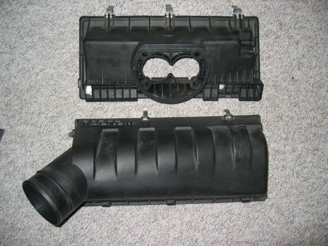 Two black plastic air cleaner housing components on a carpeted surface