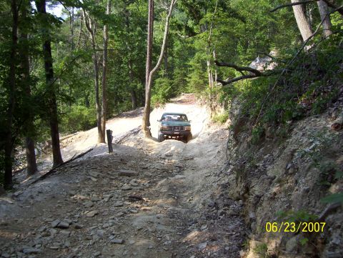 1978 Ford Bronco - A Ford Bronco navigates a challenging off-road path through a dense forest.