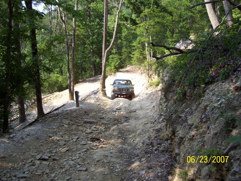 Green Ford Bronco driving up a rocky, wooded trail. Date stamp shows 06/23/2007