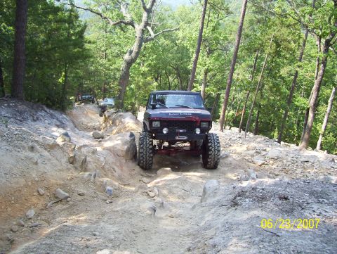 1978 Ford Bronco - A lifted 1978 Ford Bronco navigates a challenging, rocky path through a wooded area.