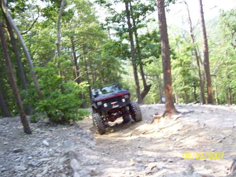 1978 Ford Bronco - An off-road vehicle navigates a rocky trail through a wooded area on a sunny day.