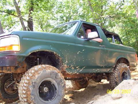1978 Ford Bronco - Mud-covered SUV navigates an off-road trail on a sunny day.