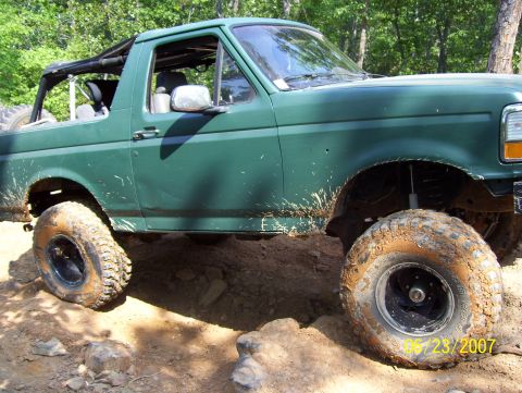 1978 Ford Bronco - This green SUV is navigating a challenging, muddy, and rocky off-road course.