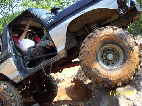 1978 Ford Bronco - A modified Ford Bronco is shown off-roading on a sunny day, with a person inside the vehicle.
