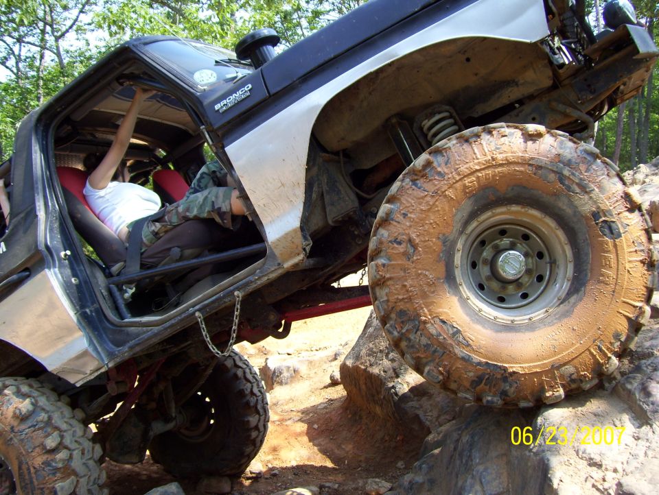 Silver and black Ford Bronco with red interior, lifted on large tires, navigating rocky terrain