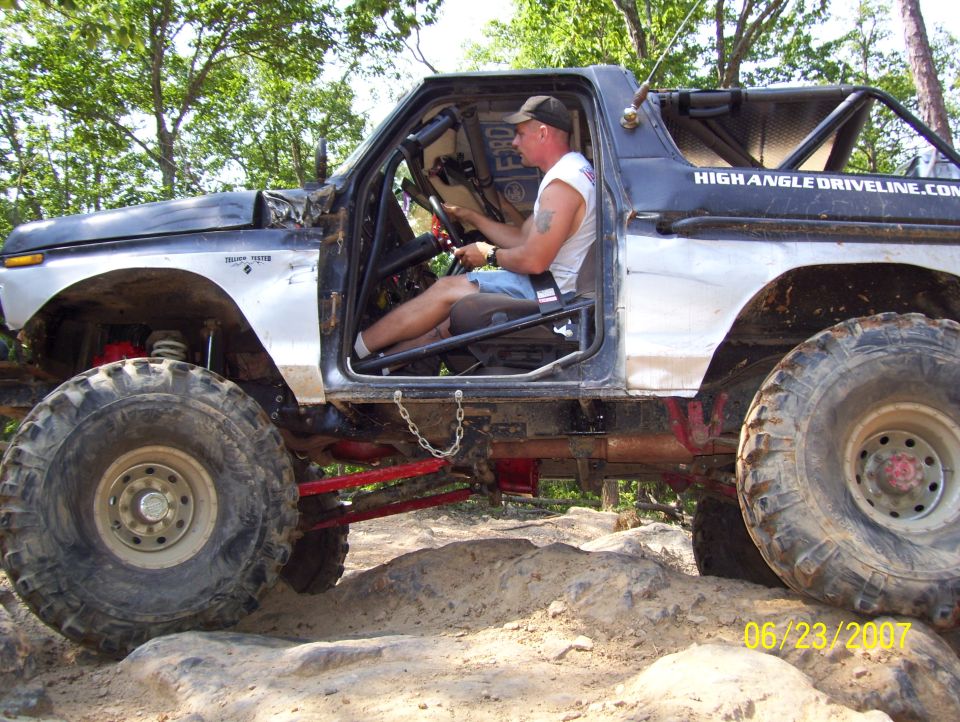 1978 Ford Bronco, silver and black, modified for off-roading, driver visible inside, on rocky terrain