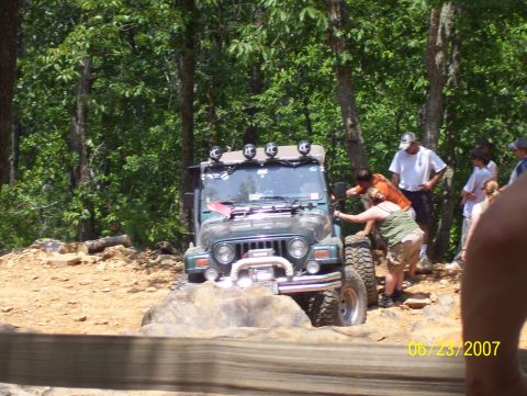 1978 Ford Bronco - A green Jeep Wrangler tackles a challenging off-road course with onlookers observing the action.