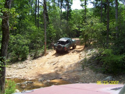 1978 Ford Bronco - 1978 Ford Bronco navigating a challenging off-road path through a forest.