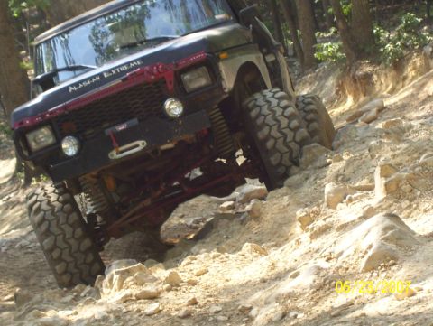 1978 Ford Bronco - This modified off-road vehicle navigates a challenging, rocky terrain on a wooded trail.