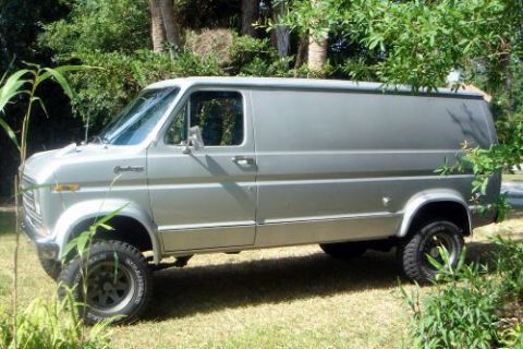 1978 Ford E250 - Driver-side profile of a silver/grey Ford Econoline panel van with solid blank sides, chrome side molding and body-side script badge, parke…