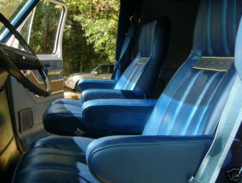 1978 Ford E250 - The interior of a van features blue vinyl bucket seats with armrests and seatbelts. Another vehicle is parked outside.