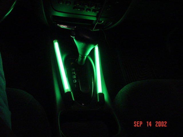 Car center console at night with green neon lights flanking an automatic shifter