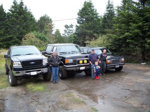 1990 Ford Bronco - Four vehicles and a group of people pose for a photo on a muddy lot.