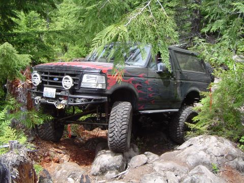 1989 Ford Bronco - This lifted Ford Bronco navigates a rocky, wooded trail with large off-road tires.