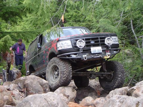 1989 Ford Bronco - A modified black Ford Bronco navigates a rocky trail with a person standing nearby.