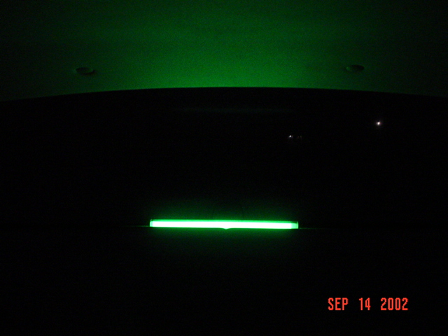 Green neon tube glowing on a car in the dark, with green light reflected on the ceiling; dated SEP 14 2002