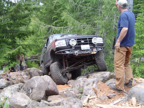 1989 Ford Bronco - A 1989 Ford Bronco tackles a challenging off-road course, its front wheels high over large rocks.