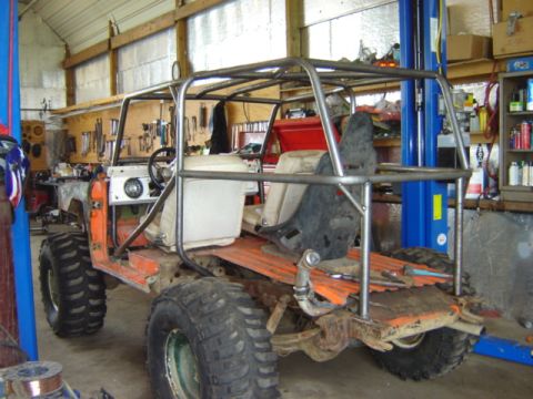1992 Ford Bronco - This heavily modified off-road vehicle features a custom roll cage and oversized tires, seen in a workshop setting.