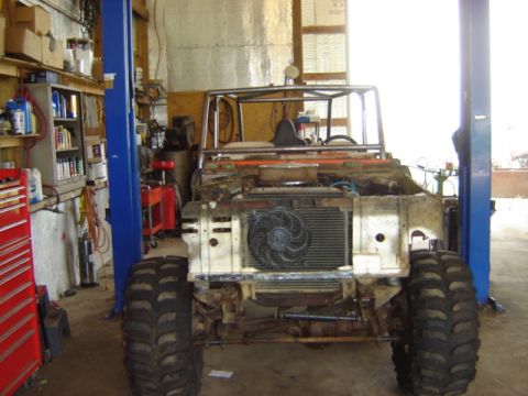1992 Ford Bronco - This heavily modified Ford Bronco is in a workshop, showing its front end with large tires and a roll cage.