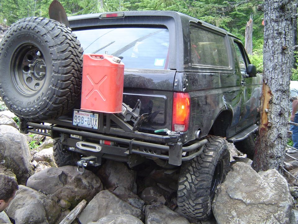Black Ford Bronco rear view on rocks with spare tire, red gas can, and winch bumper