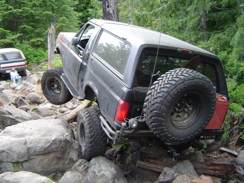 1989 Ford Bronco - A modified Ford Bronco tackles a challenging rocky terrain, with another SUV visible in the background.