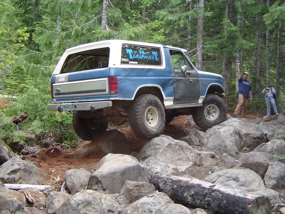 Blue and white Ford Bronco climbing rocks on a forest off-road trail