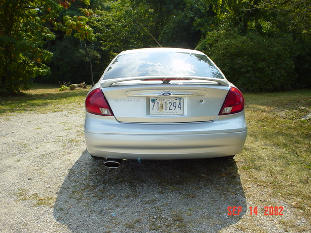 Rear view of a silver Ford Taurus SEL sedan with spoiler and Indiana plate on a gravel driveway