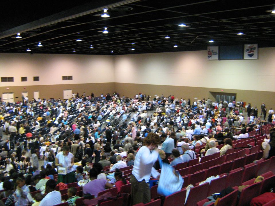 Crowd filling tiered red seating in a large convention arena