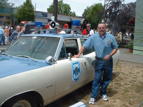 2000 Ford Crown Victoria - A man stands by a vintage Seattle Police car, which has a two-tone paint scheme and emergency lights.