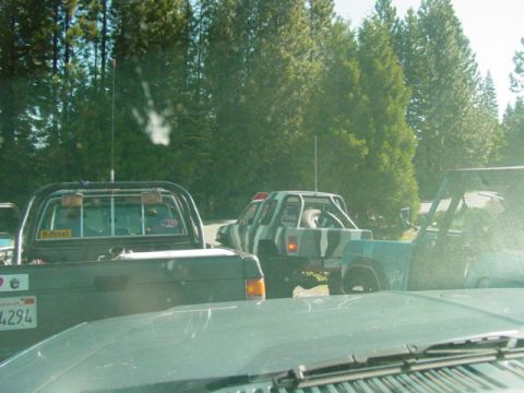 1986 Ford Bronco - A camouflaged SUV with a roll cage is seen from behind, towing a trailer, with other vehicles in the foreground.