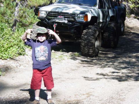 1986 Ford Bronco - A child poses in front of a heavily modified off-road SUV, likely a Toyota 4Runner from the late 1980s.