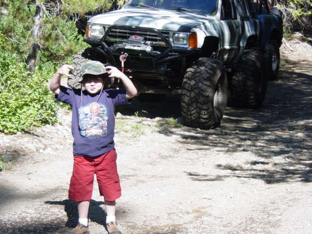 Modified off-road SUV with large tires and a child standing in front. The SUV appears to be from the late 1980s