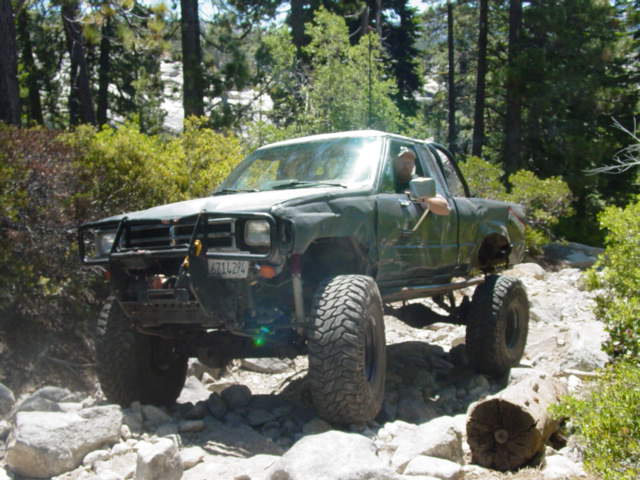 Green off-road truck with large tires navigating rocky terrain