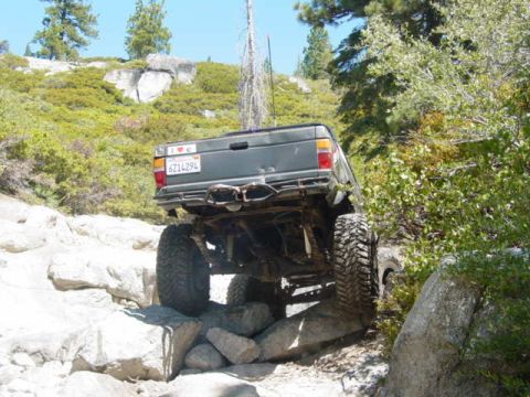 1986 Ford Bronco - A dark green SUV is shown off-roading over large rocks on a sunny day.