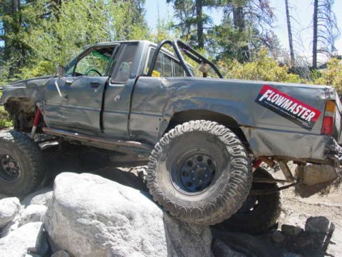 1986 Ford Bronco - Modified pickup truck navigates rocky terrain with large tires and roll cage.